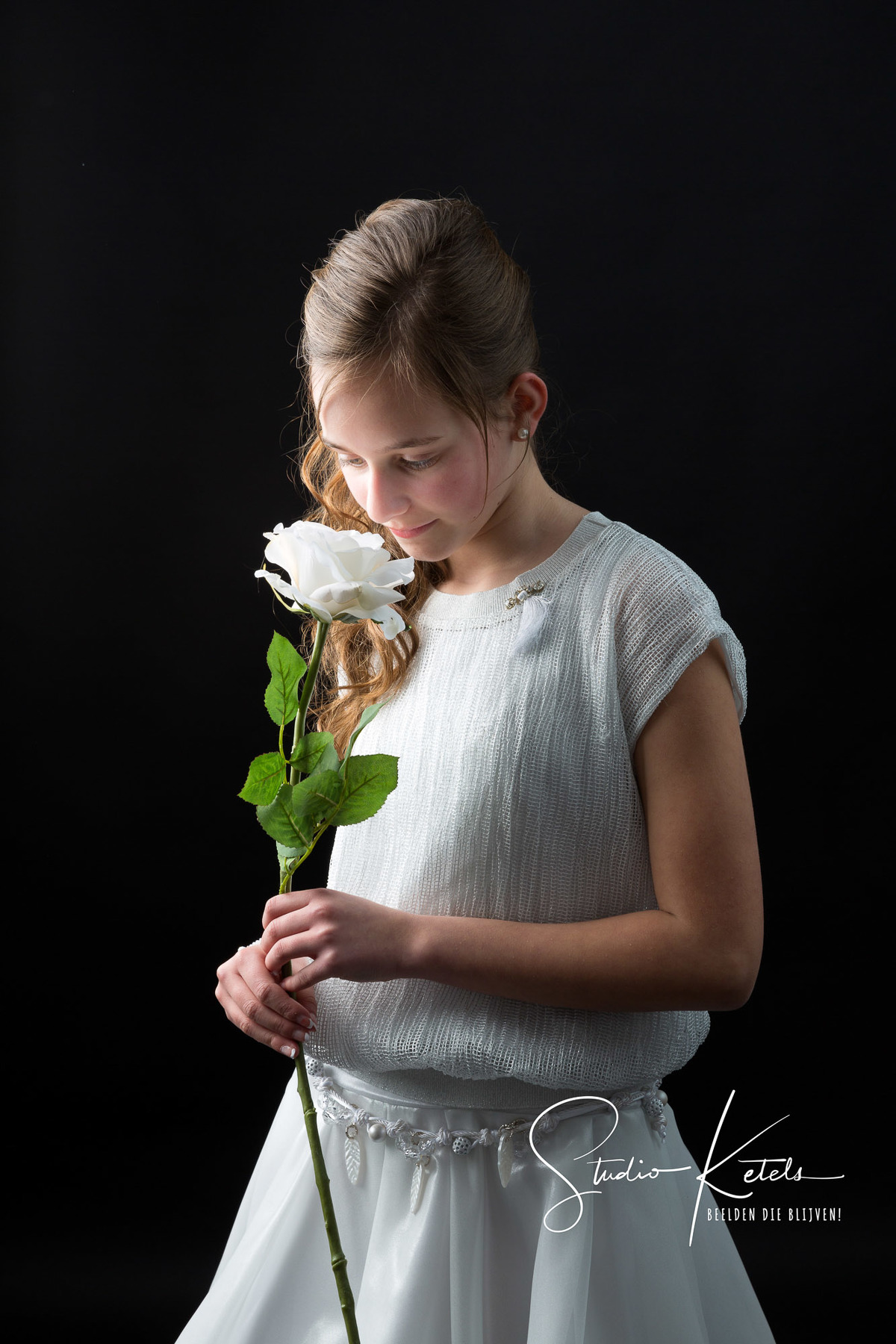 Communieportret van een meisje. Ze heeft een witte bloem in haar hand, en ruikt eraan. Portret door Studio Ketels